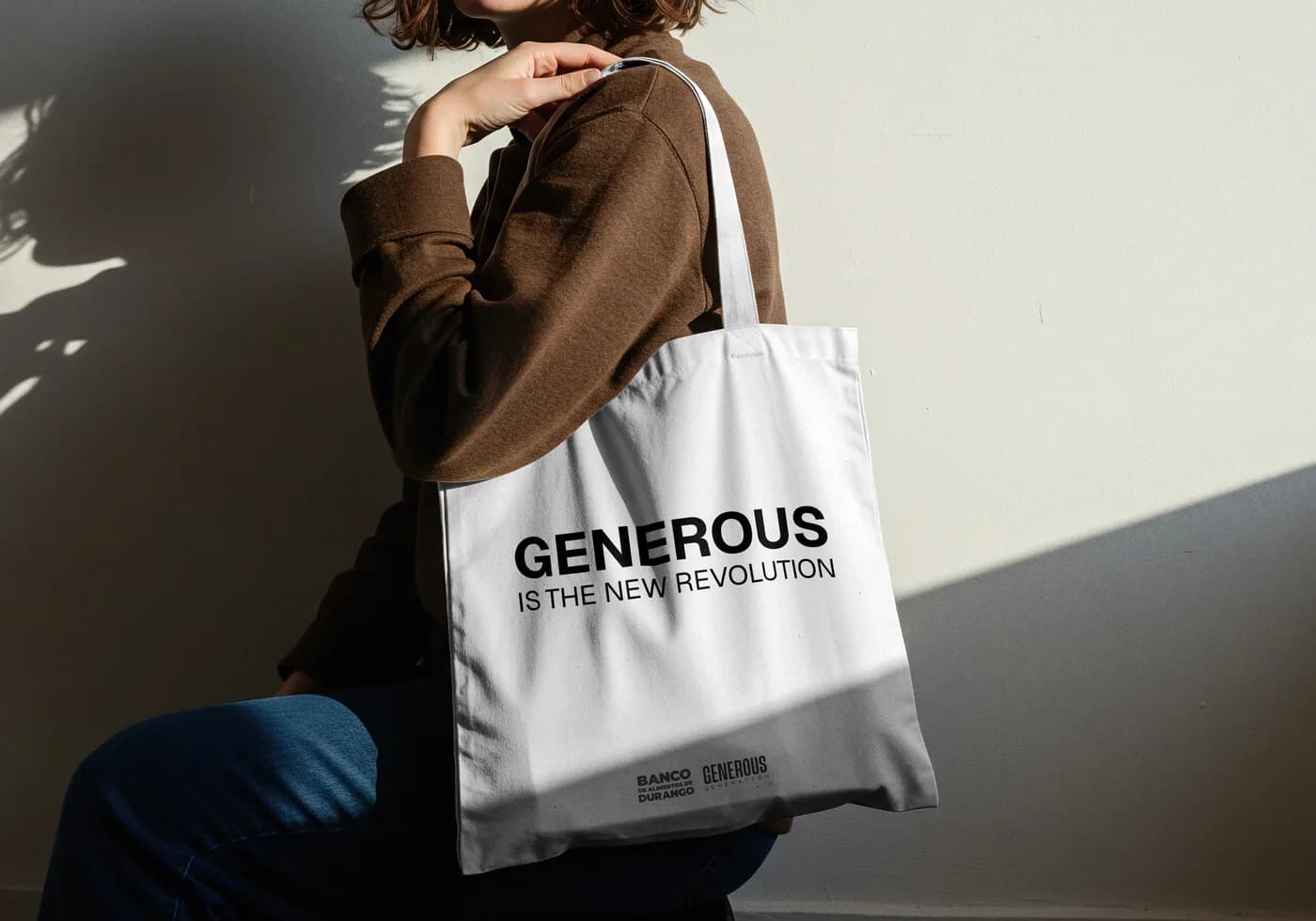 Tote bag blanco con la leyenda Generous is the new revolution, colgado del hombro